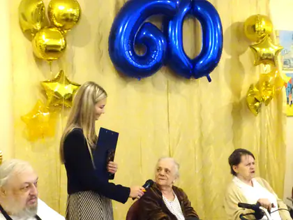 Prowadząca z mikrofonem rozmawia z mieszkankami na tle złotych balonów i niebieskiego balonu 60