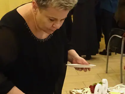 Kobieta kroi tort z cyfrą 60, w tle goście