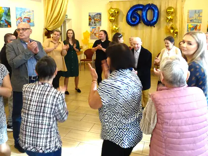 Goście klaszczą w sali udekorowanej niebieskimi i złotymi balonami z liczbą 60