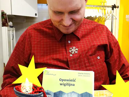 Mężczyzna na wózku trzyma książkę Opowieść wigilijna i świecznik, obok żółte gwiazdy