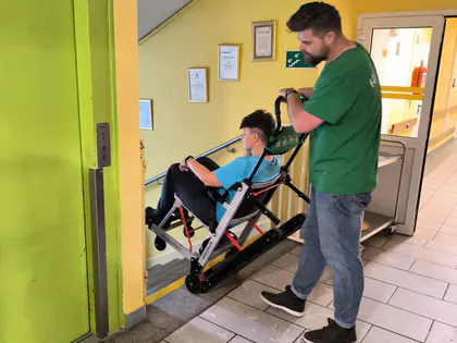 Mężczyzna przewozi osobę na krzesełku ewakuacyjnym przez korytarz