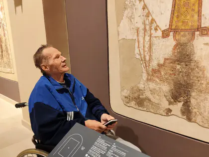 Mężczyzna na wózku ogląda średniowieczny fresk na ścianie muzeum