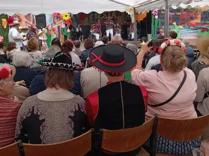 Publiczność w sombrerach i kwiatowych wiankach ogląda występ na scenie pod namiotem
