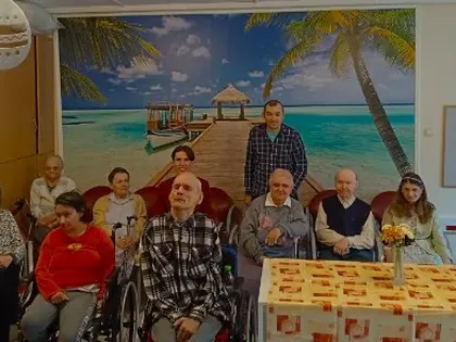 Mieszkańcy i młodzi goście siedzą w sali z plakatem tropikalnej plaży na ścianie