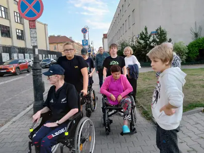 Grupa osób z mieszkańcami na wózkach spaceruje ulicą