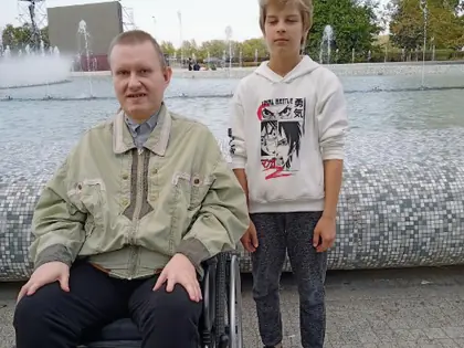 Mężczyzna na wózku i chłopiec stoją przy fontannie