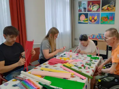 Mieszkańcy i młodzież robią kwiaty z bibuły przy stole