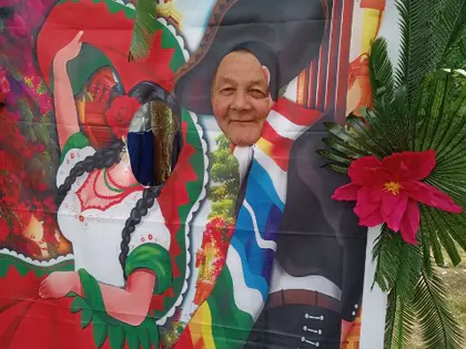 Mieszkanka wkłada twarz w otwór kolorowej ścianki z tancerzami meksykańskimi