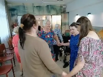 Grupa osób tańczy w kole, trzymając się za ręce