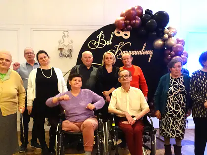 Mieszkańcy i pracownicy pozują przed dekoracją z balonami i napisem Bal Karnawałowy