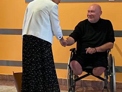 Kobieta w białym żakiecie wita się z mężczyzną na wózku w holu