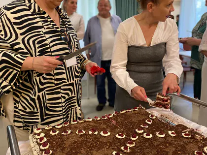 Dwie kobiety kroją prostokątny tort czekoladowy ozdobiony wiśniami