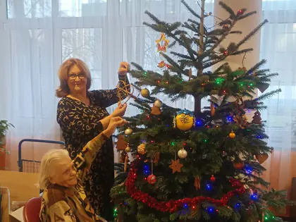 Kobieta wiesza ozdoby na żywej choince, obok siedzi mieszkanka