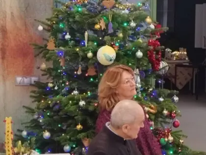 Kobieta i ksiądz w czarnej sutannie siedzą przy ustrojonej choince