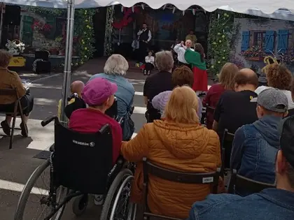 Osoby na wózkach inwalidzkich patrzą na scenę, z boku inne osoby