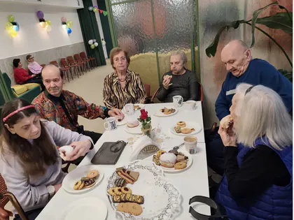 Mieszkańcy jedzą ciastka i pączki przy stole z różą w wazonie