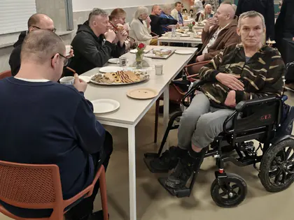 Mieszkańcy przy białym stole z talerzem ciastek, jeden mężczyzna na wózku patrzy w obiektyw