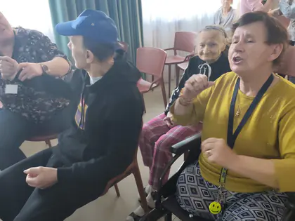 Opiekunki i mieszkańcy śpiewają siedząc w kręgu