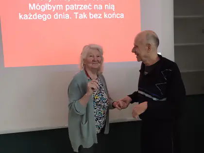 Mieszkanka i mieszkaniec tańczą przed ekranem z tekstem piosenki