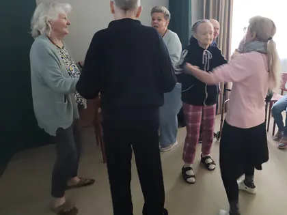 Mieszkańcy i młodzież tańczą w parach w sali z zielonymi zasłonami