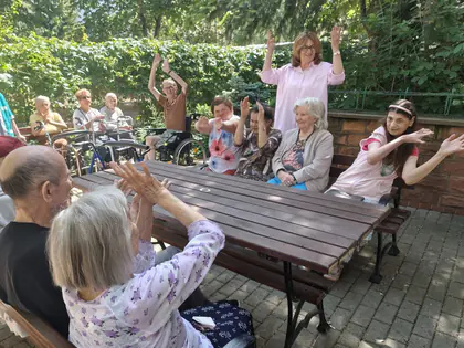 Mieszkańcy unoszą ręce podczas wspólnego śpiewu w ogrodzie