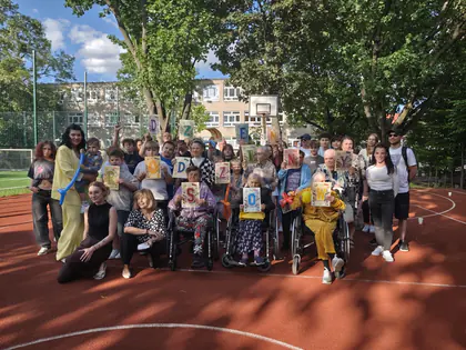 Duża grupa mieszkańców i gości pozuje z literami na boisku