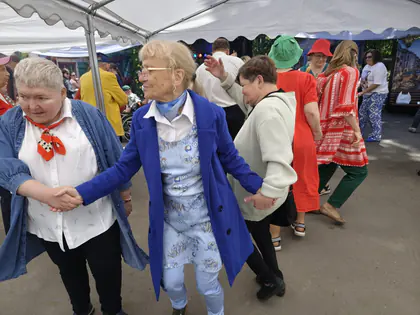 Mieszkanki tańczą trzymając się za ręce na festynie