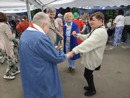 Trzy panie tańczą, trzymając się za ręce, wokół bawią się inne osoby