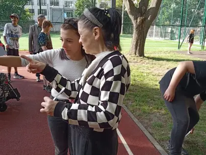 Dwie kobiety rozmawiają ze sobą, wskazując palcami, w tle boisko szkolne
