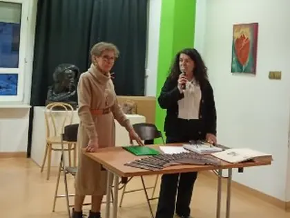 Dwie kobiety prowadzą spotkanie w sali Tyflogalerii, jedna mówi do mikrofonu przy stole z książkami