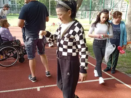 Kobieta z białym plastikowym kubkiem idzie po boisku, w tle młodzi zawodnicy
