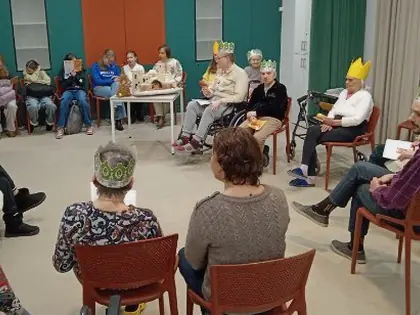 Mieszkańcy i młodzież w papierowych koronach siedzą w kręgu i śpiewają kolędy