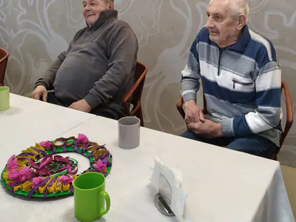 Dwaj starsi panowie w dobrym nastroju siedzą przy białym stole z zastawą i stroikiem wielkanocnym
